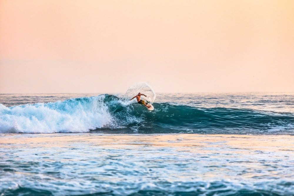 Mann reitet Wellen auf Surfbrett. Wie viel kostet eine Reise nach Hawaii? Urlaub auf Hawaii