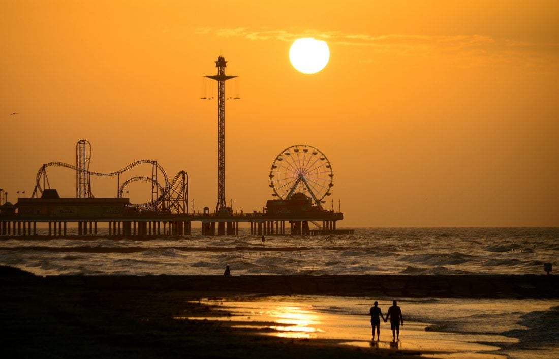 A couple walking along the water on a beach during sunset near Galveston Island's Pleasure Pier