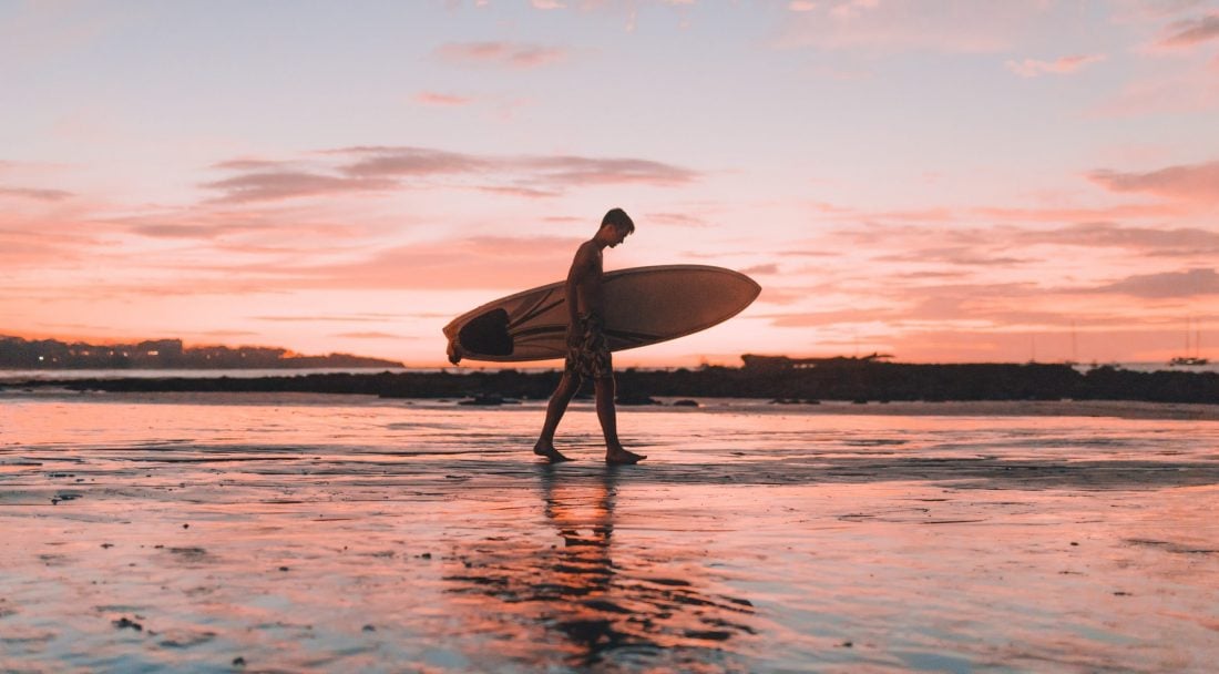 A man walking to catch some surf during a sunset at a beach in Bali