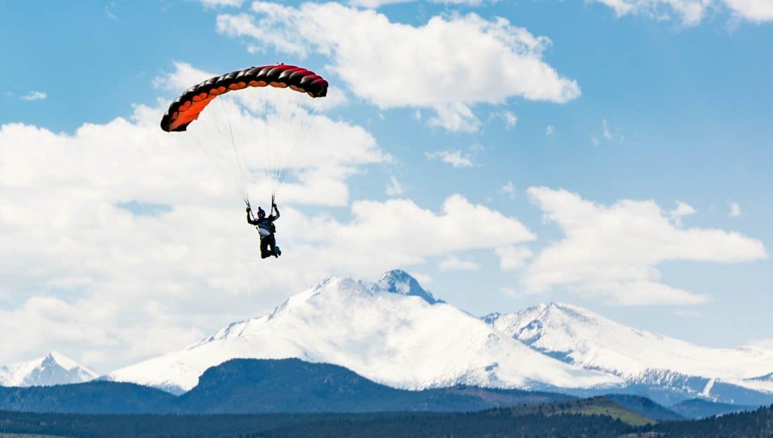 a skydiver floats down with chute deployed with the Rockies in the background in Longmont. Photo courtesy the Mile Hi Skydiving Center