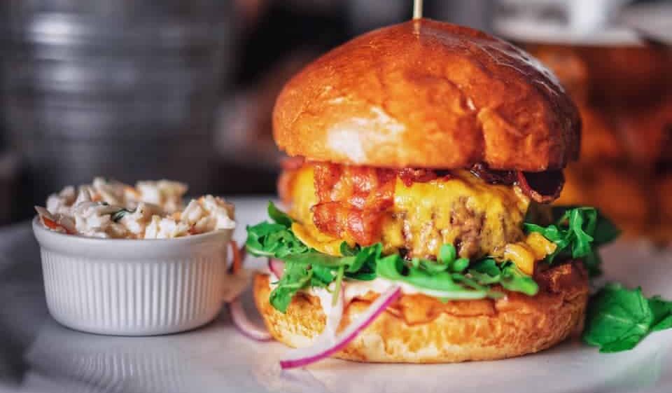 A cheeseburger and a cup of slaw on a plate.
