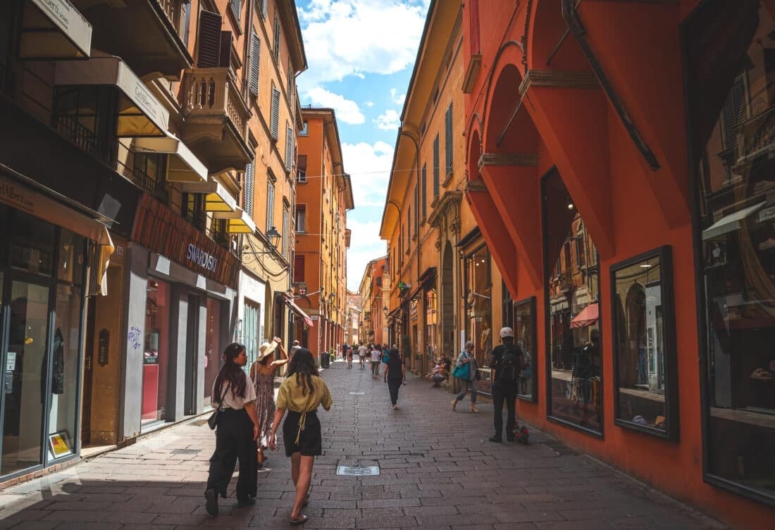 People walking down a orange and red hued street in Bologa, Italy. 