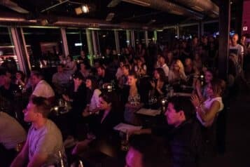 Fans seated and standing around the large windows at Jazz Dock, one of the best live music venues in Prague on the river. 