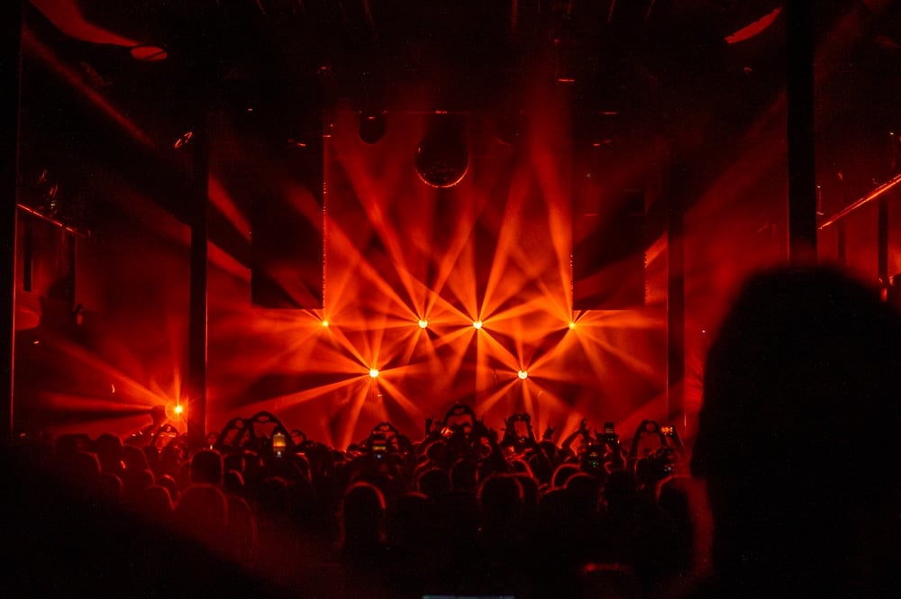 Red stage lighting and fans holding hearts in the air during Our Last Night's set at SaSaZu