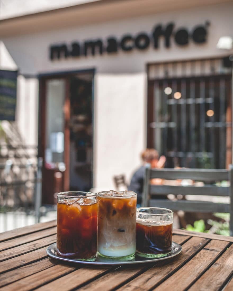 Three glasses of iced coffee on a table in front of the mamacoffee entrance, one of the best Prague alternatives to Starbucks. 