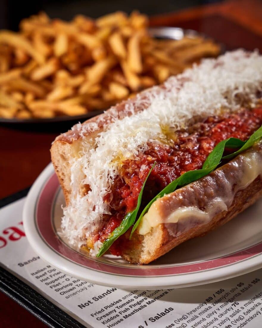 The meatball sub topped with parmesan cheese and fries in the background at Sandwich Rodeo, the best Prague alternative to a diner sandwich.