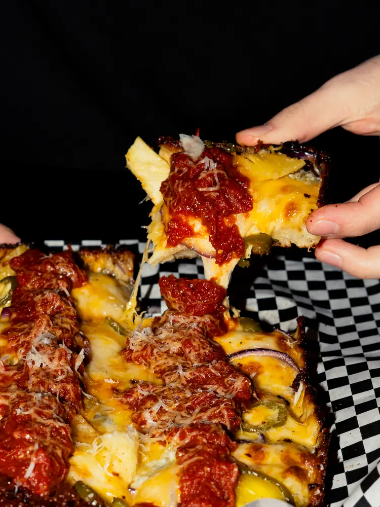 Someone pulling a piece of pizza away from the pie at Third Coast Pizza.